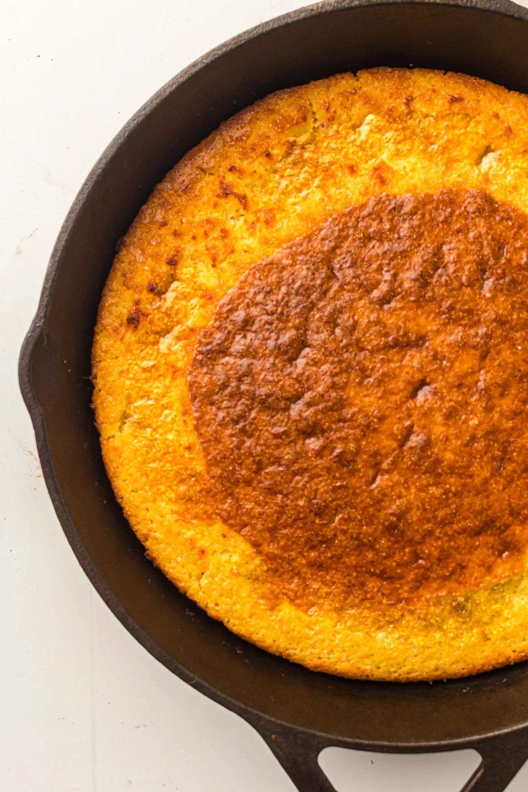 The finished golden round loaf sitting in a black cast iron pan