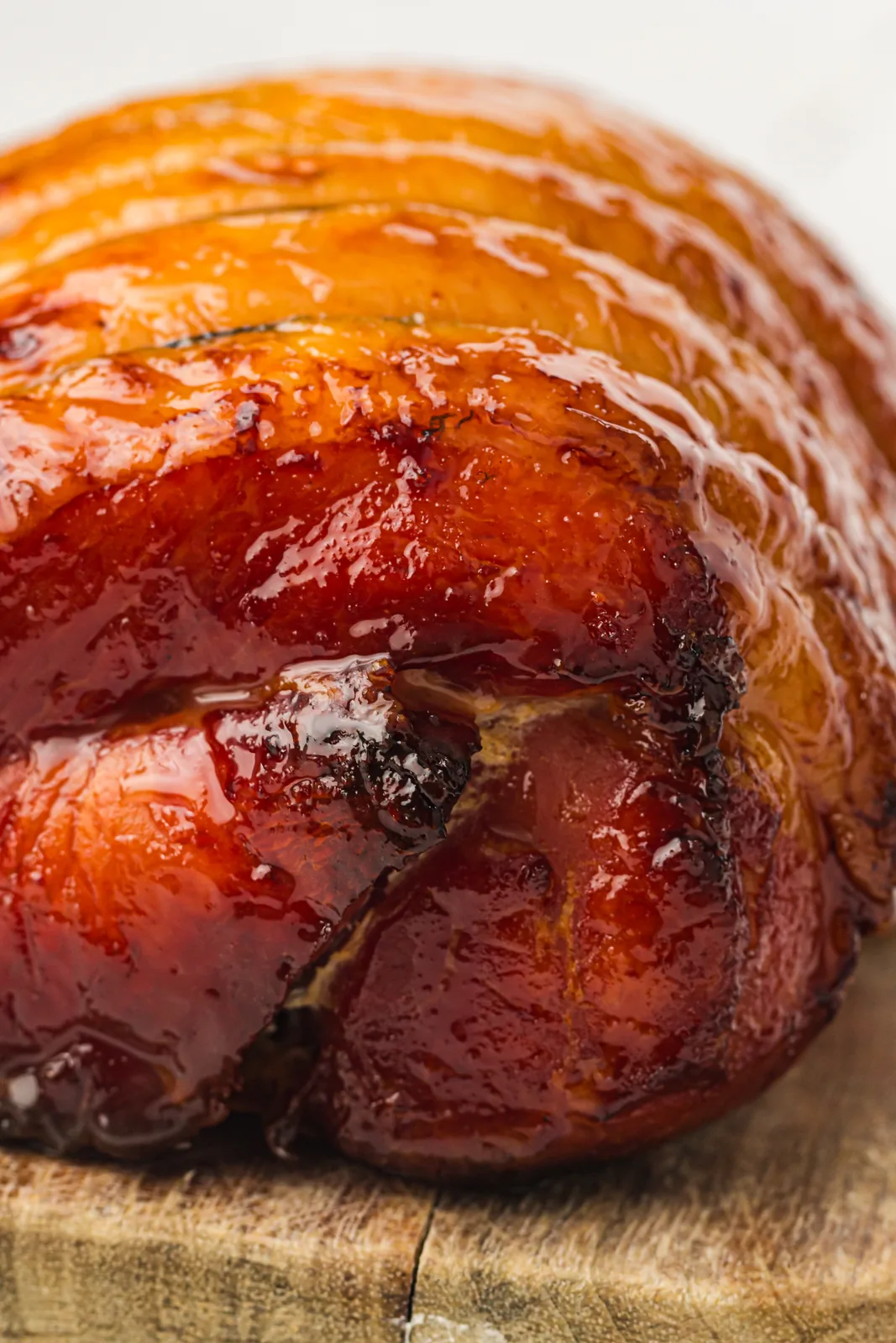A whole honey glazed ham with a deep mahogany lacquer resting on a wooden board