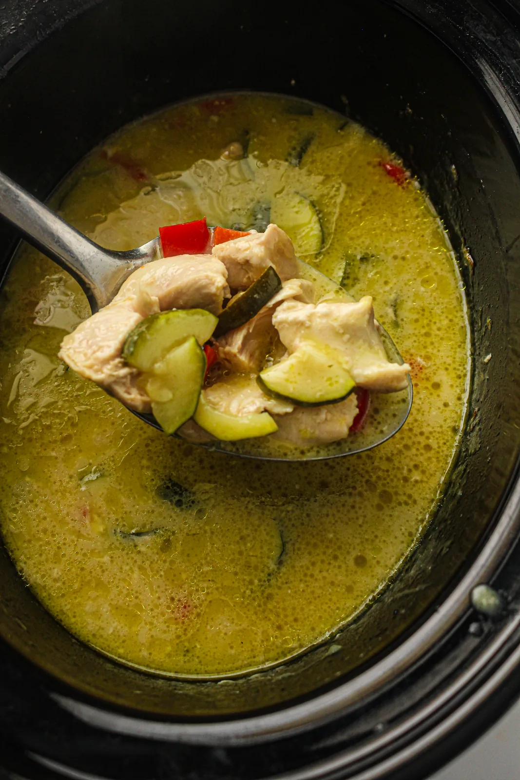 A ladle lifting courgette and tender chunks from the pale green sauce