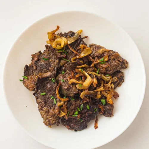 Old-fashioned liver and onions on a white plate with golden fried onions and parsley