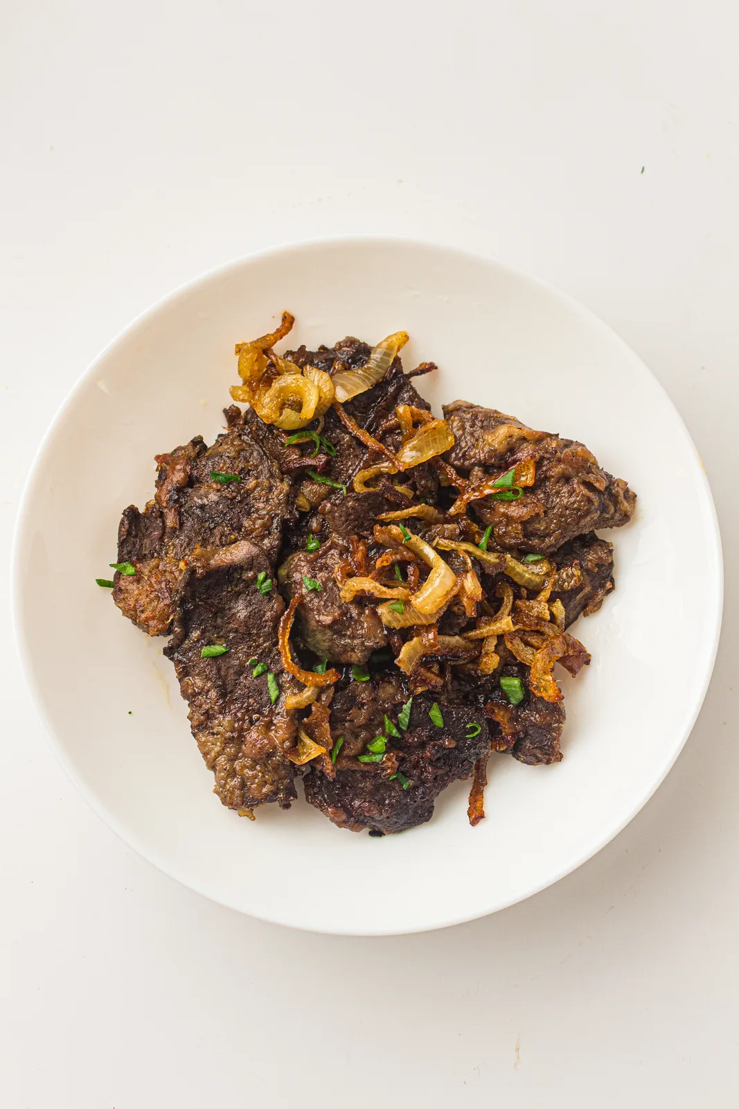 Old-fashioned liver and onions on a white plate with golden fried onions and parsley