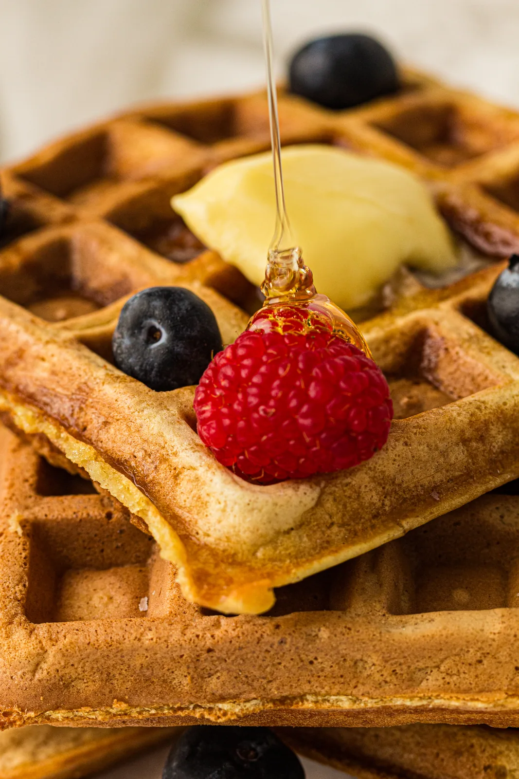 Maple syrup poured over a golden stack topped with a raspberry