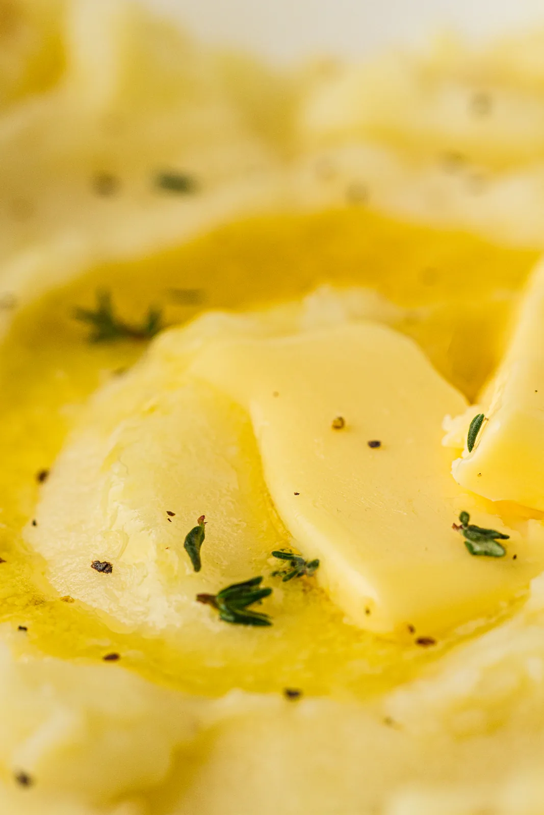Close up of melted butter and thyme leaves sinking into a creamy side dish