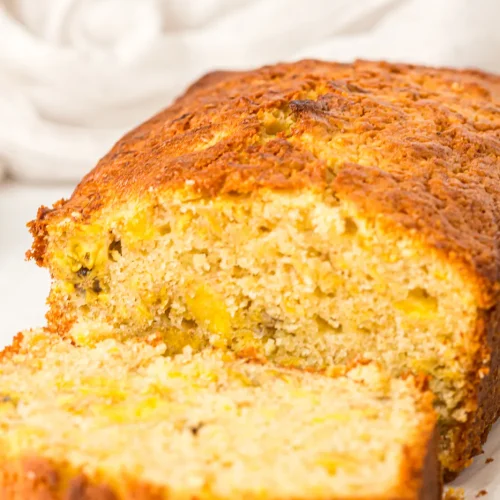 Plantain bread on parchment with a slice cut to show the flecked golden crumb
