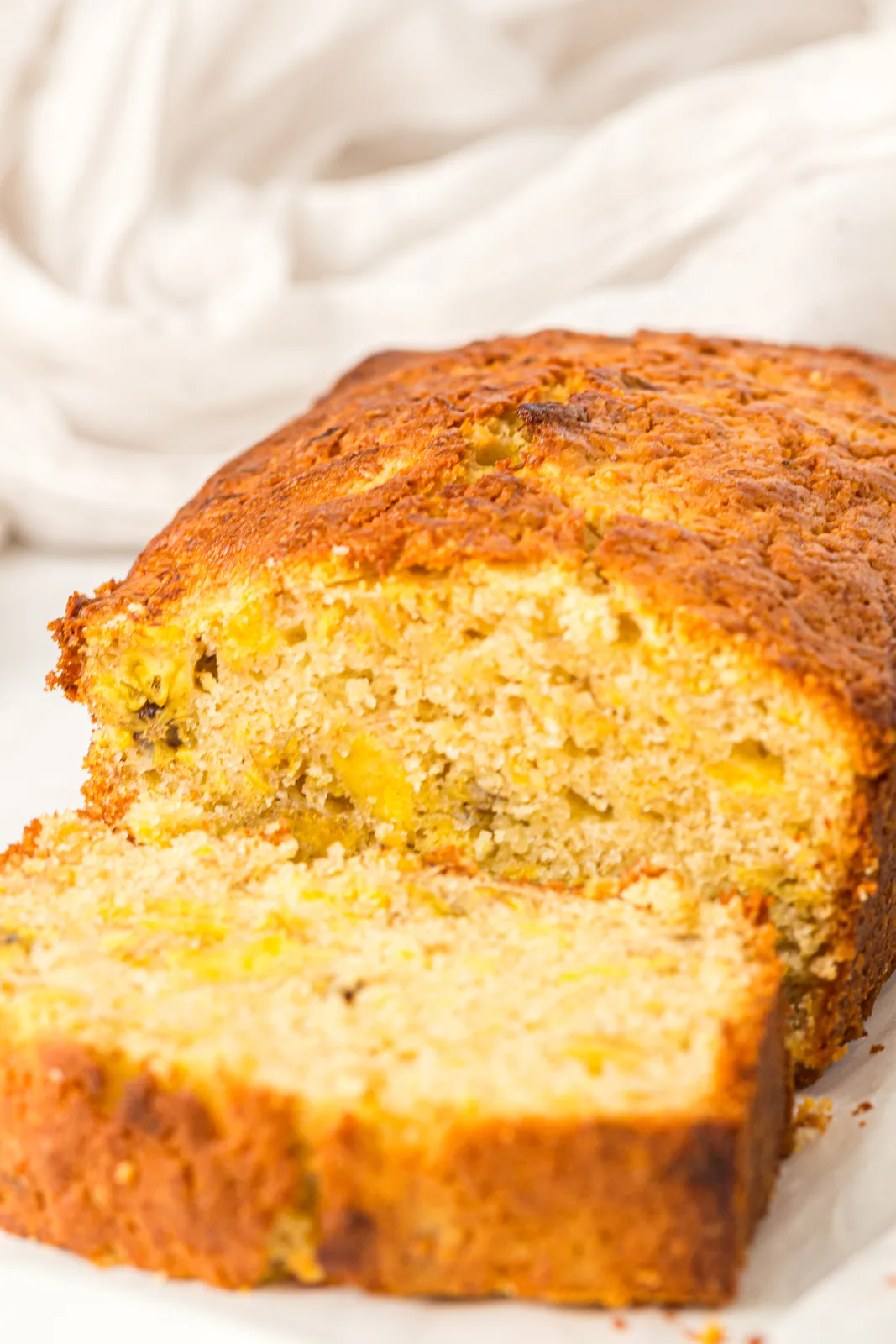Plantain bread on parchment with a slice cut to show the flecked golden crumb