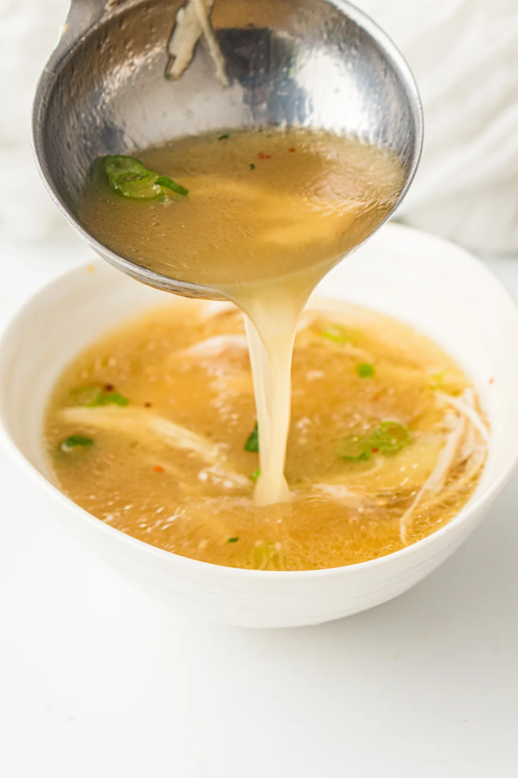 Clear golden broth being poured from a ladle into a bowl