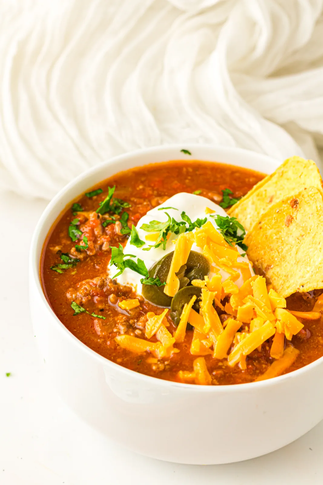 Bowl of pumpkin chili with soured cream, cheddar, jalapenos and tortilla chips