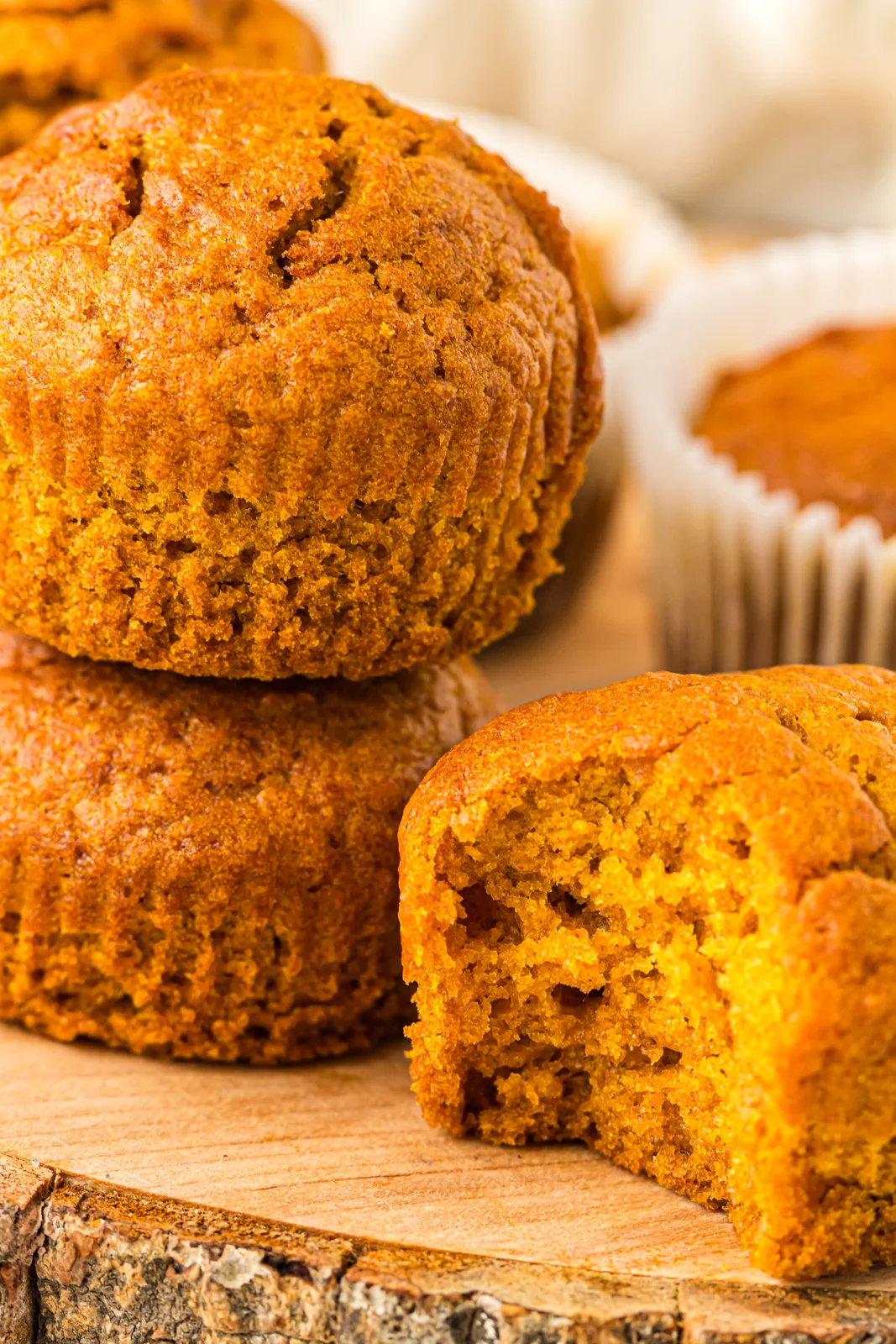 Stack of pumpkin muffins on a wooden board with one split open