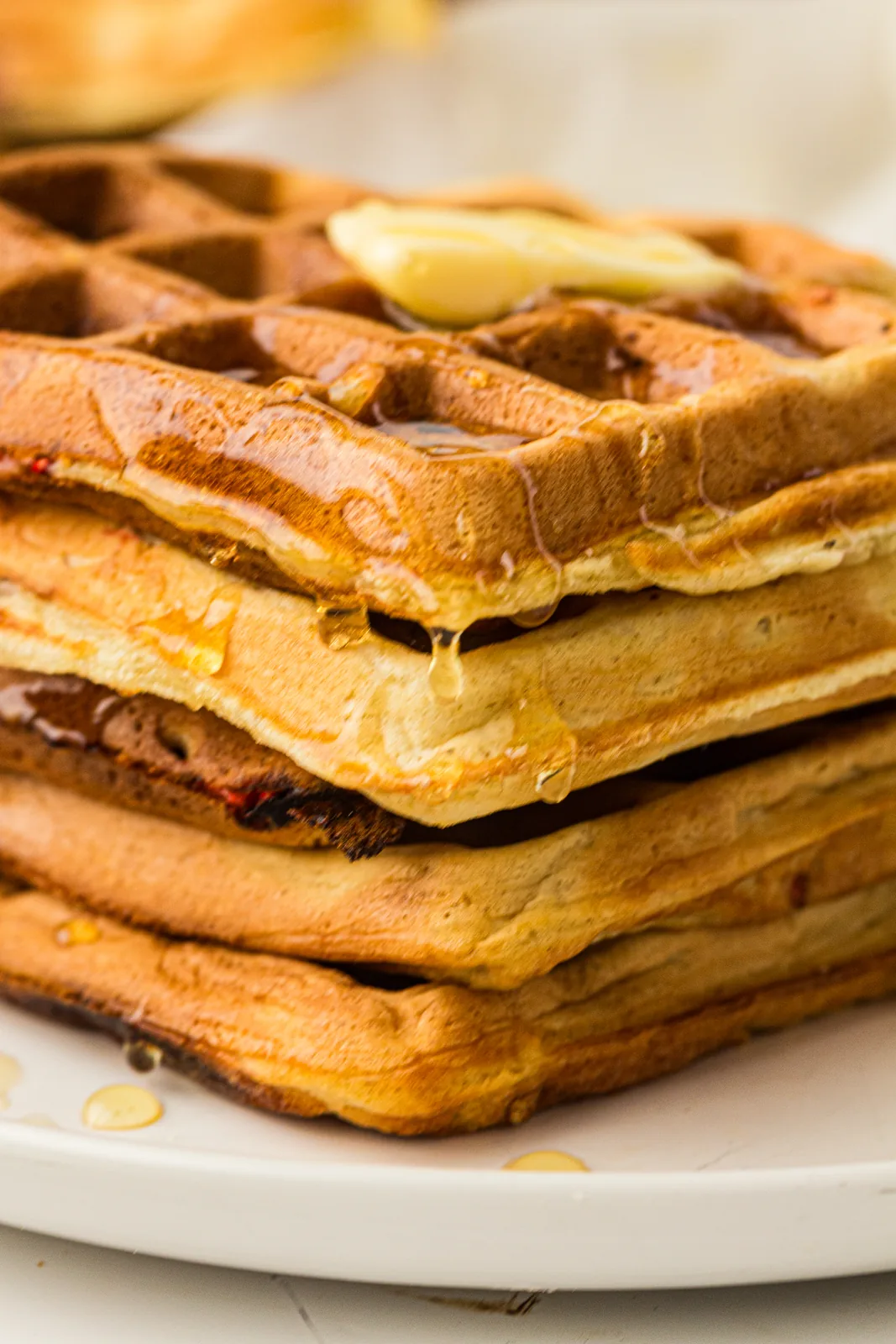 A tall stack of raspberry sourdough waffles with butter and syrup running down
