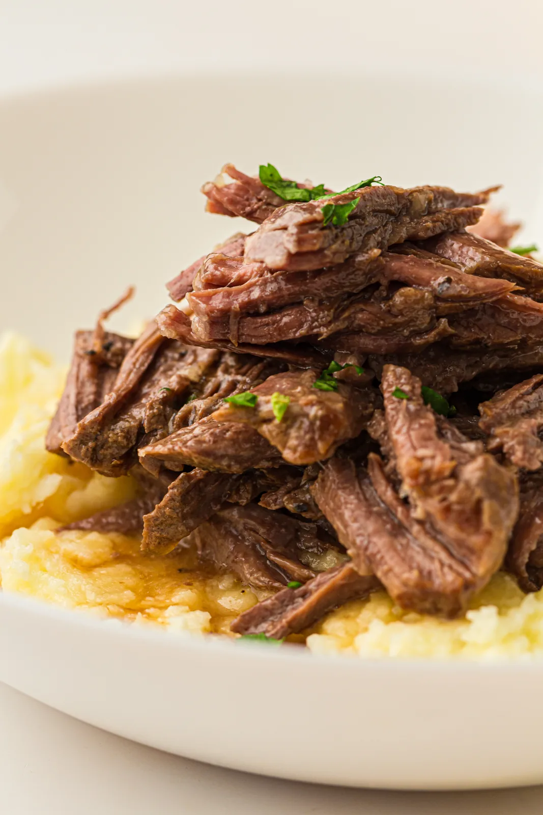 Shredded beef piled over buttery mash in a white bowl