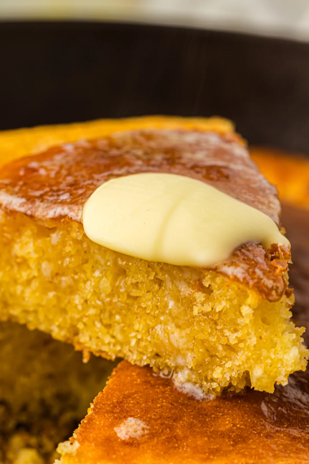 A wedge of skillet cornbread with a curl of butter melting on top