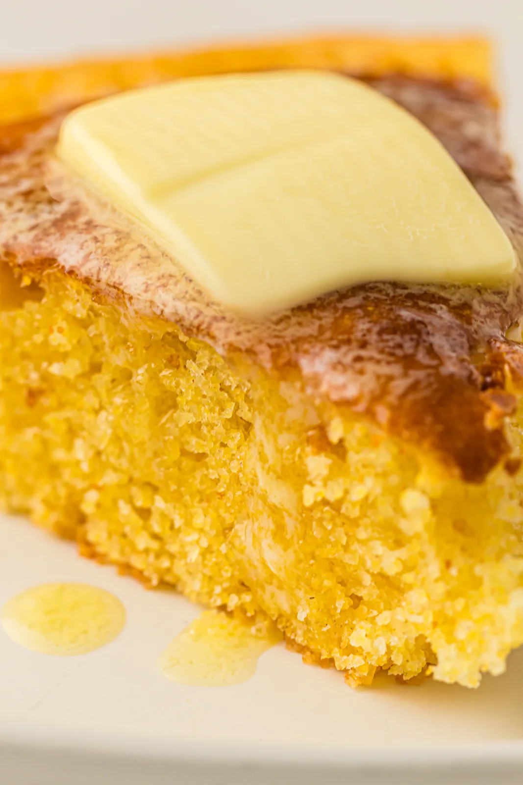 A slice on a white plate with butter melting into the warm crumb