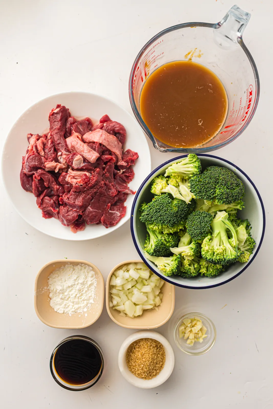 Ingredients for slow cooker beef and broccoli: sliced steak, florets, onion, garlic, stock and sauce