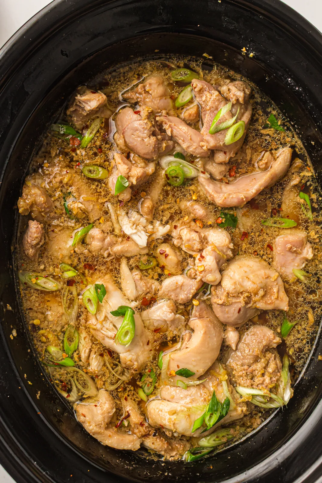 Slow cooker teriyaki chicken in the pot with spring onion and chilli flakes