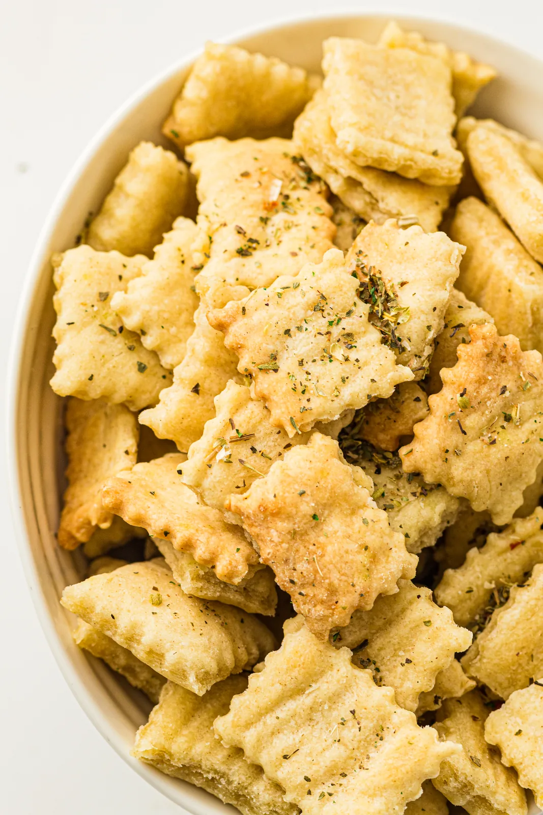 A bowl of sourdough discard crackers scattered with dried herbs