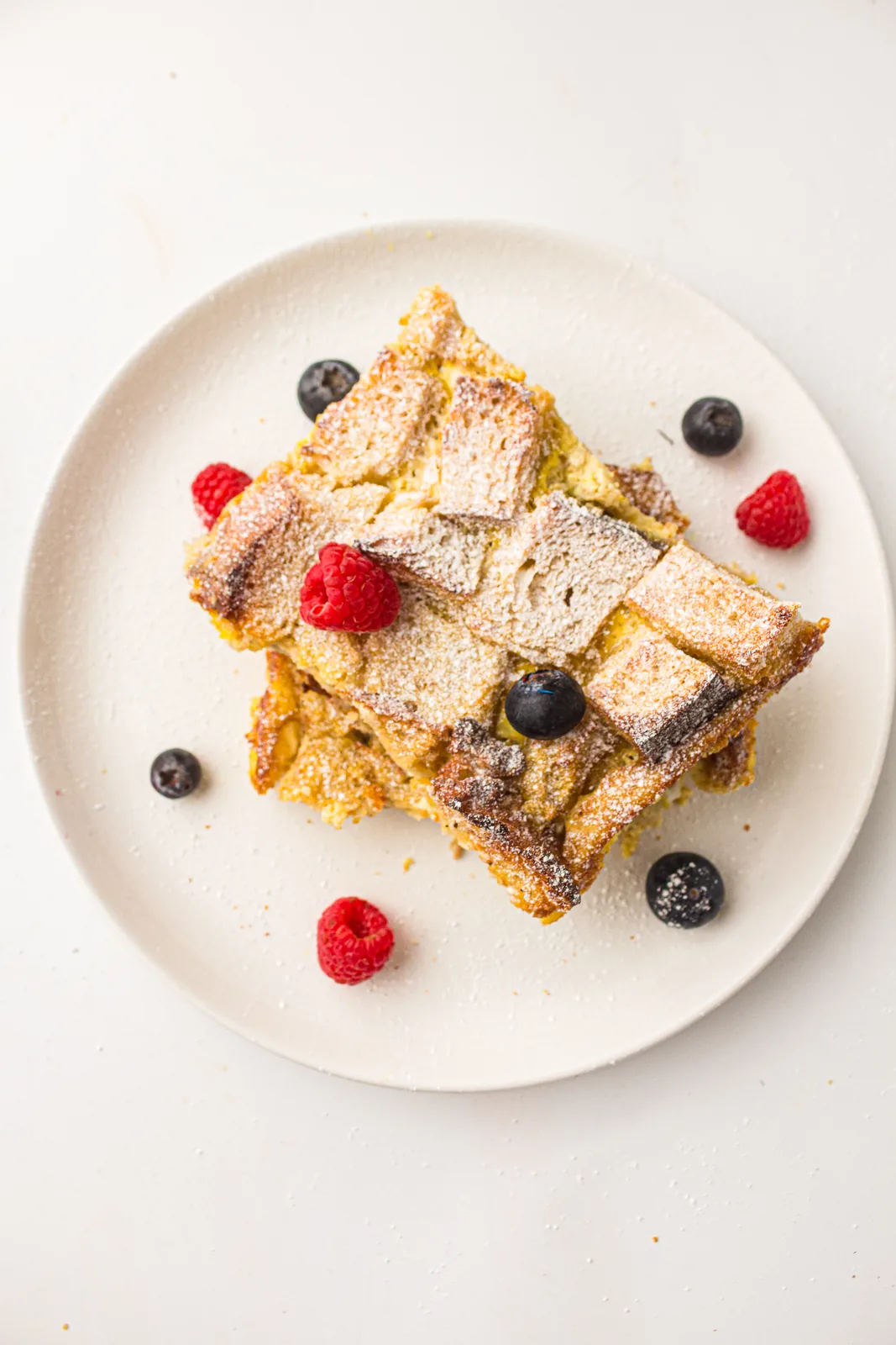 A square of sourdough french toast casserole on a plate with berries