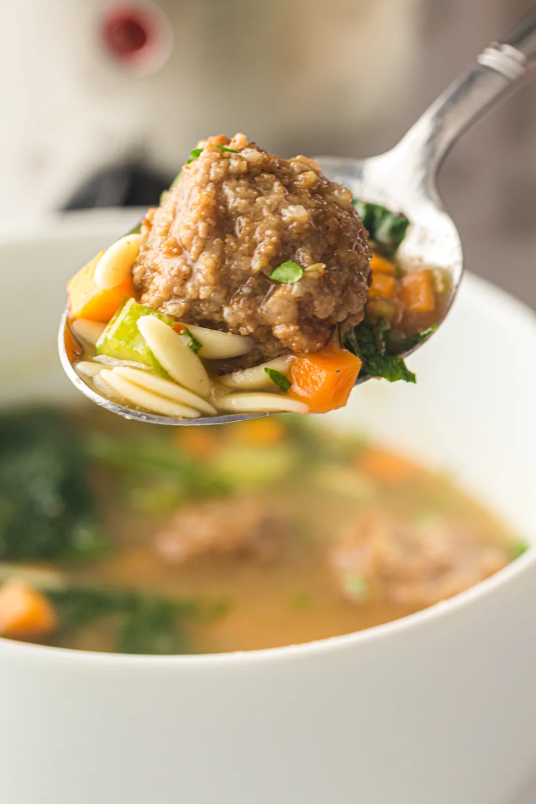 A spoon lifting a single meatball over the rim of the bowl