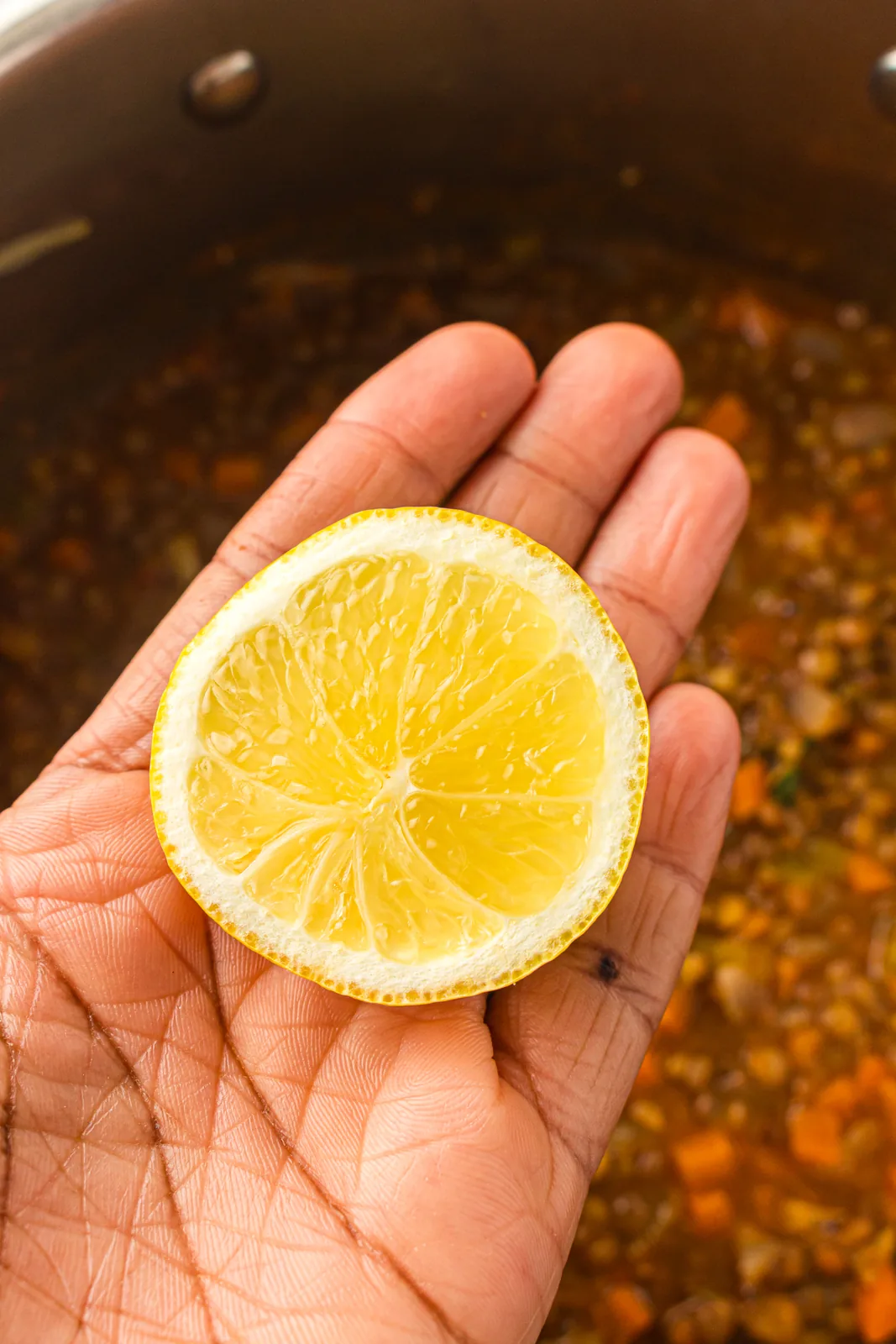 A lemon half held over the pot ready to squeeze in at the end