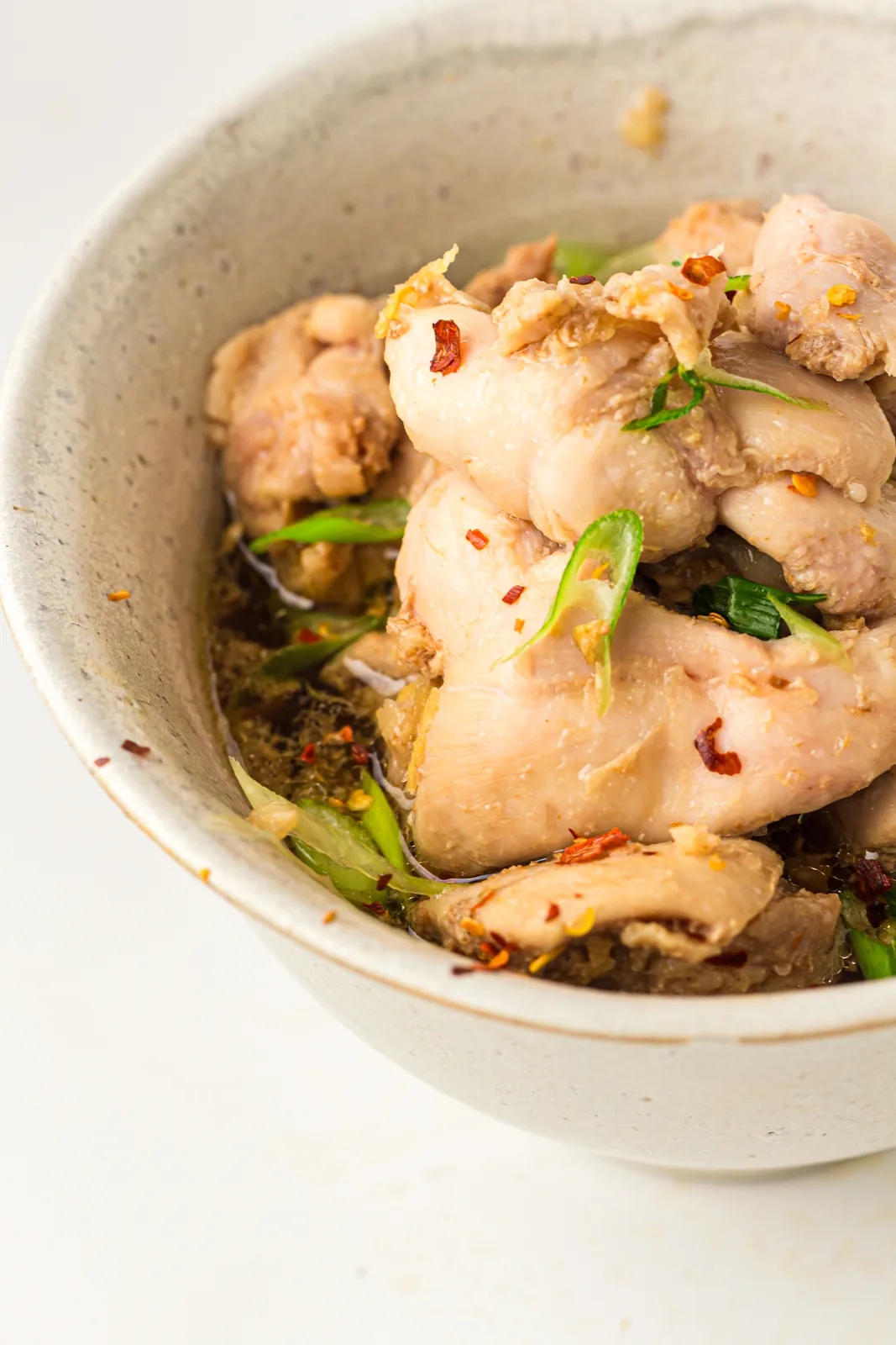 A stone bowl of glazed morsels with green onion and chilli flakes