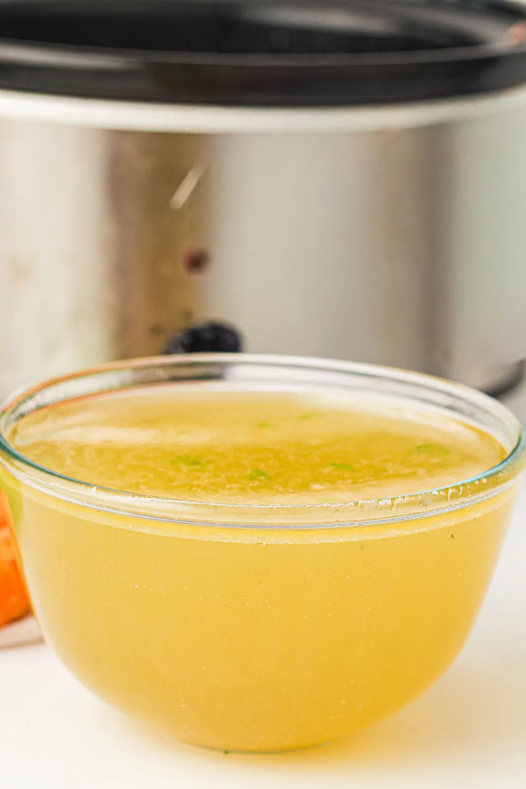 Strained golden liquid in a bowl beside the slow cooker