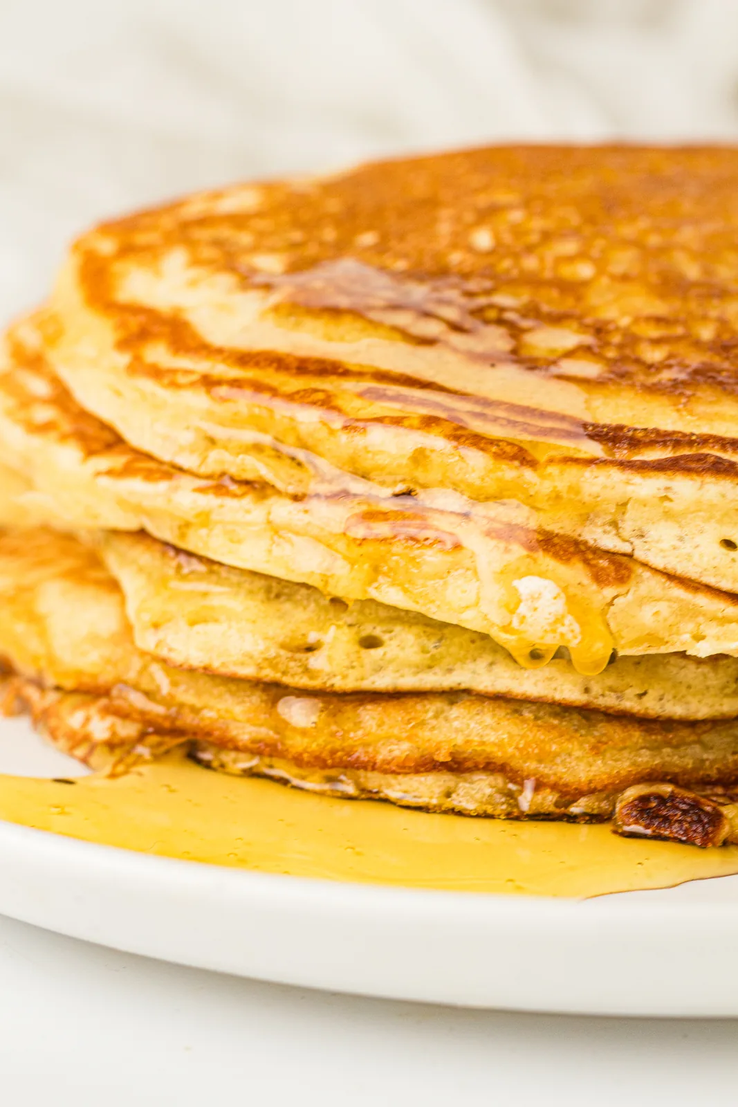 A tall golden stack with syrup running down the sides and berries scattered around
