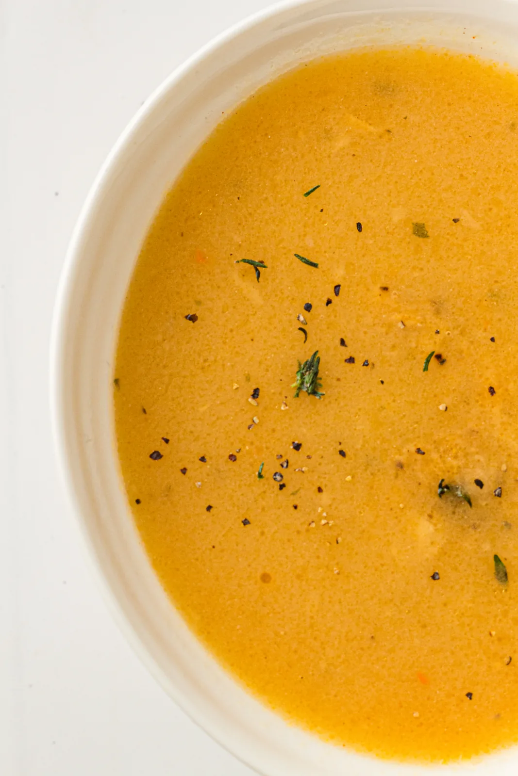 A shallow bowl of smooth golden turkey gravy flecked with black pepper and thyme