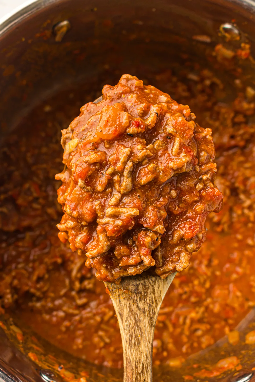 A wooden spoon lifted over the simmering pan