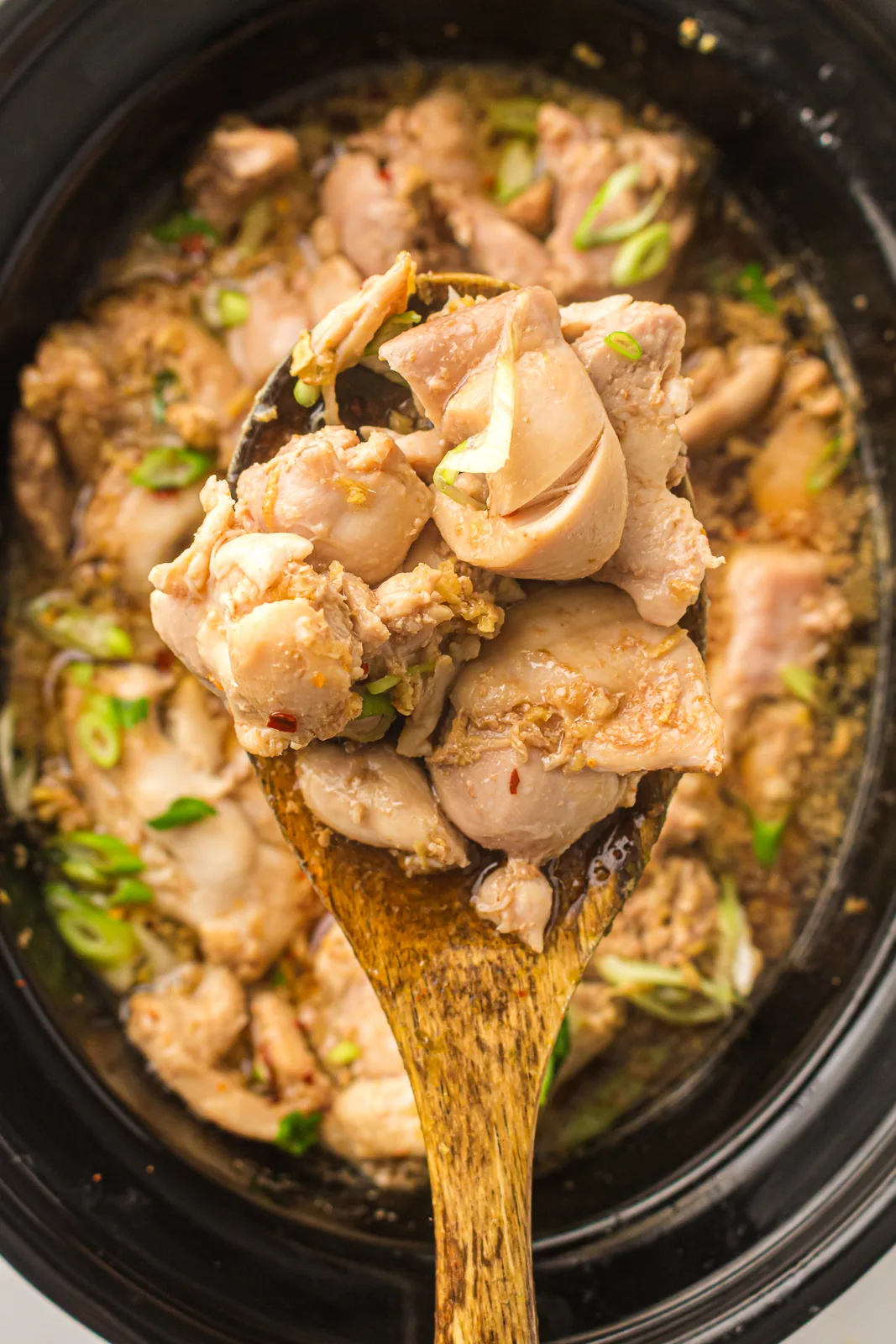 A wooden spoon lifting glazed morsels out of the dark crock