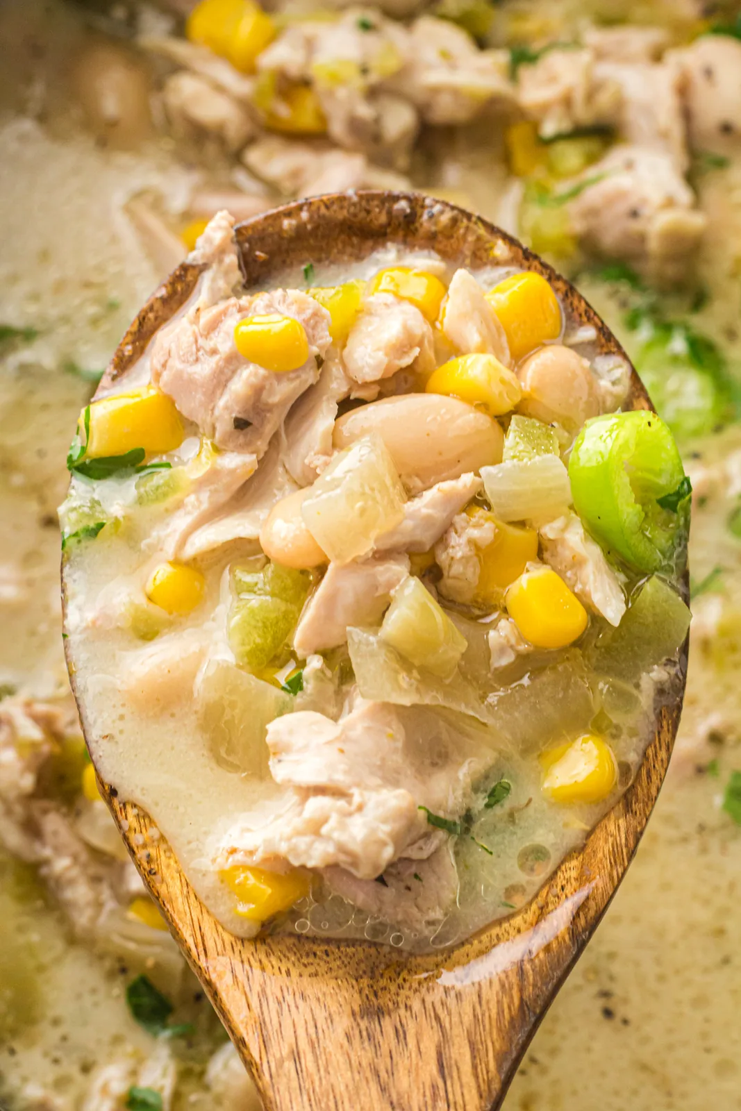 A wooden spoon holding sweetcorn, white beans and shredded meat