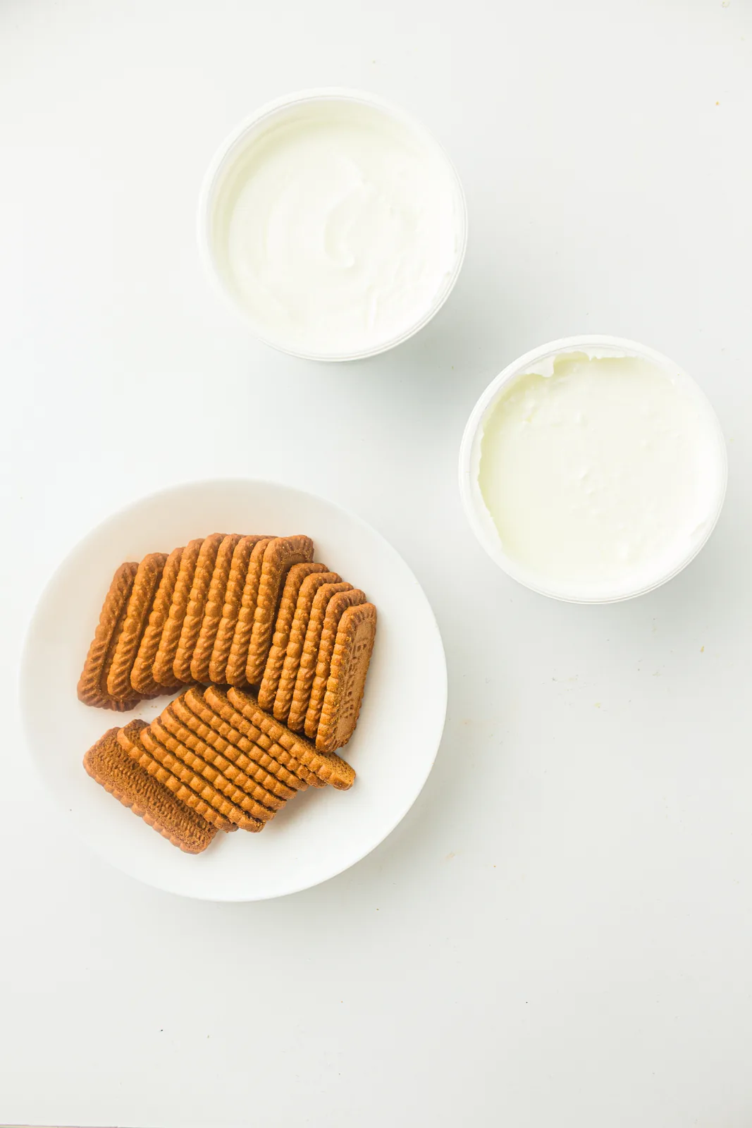 Ingredients for yogurt cheesecake: two tubs of thick white yogurt and a plate of caramel biscuits