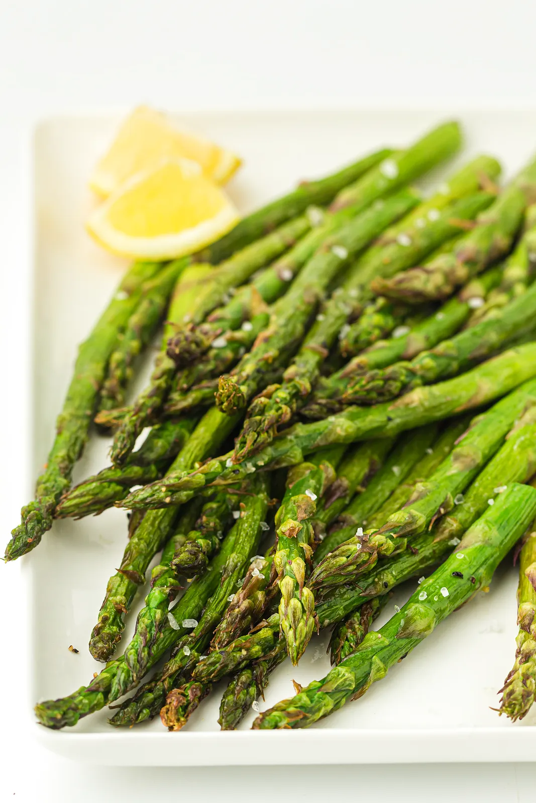 Air fryer asparagus on a white platter with lemon wedges and flaky salt