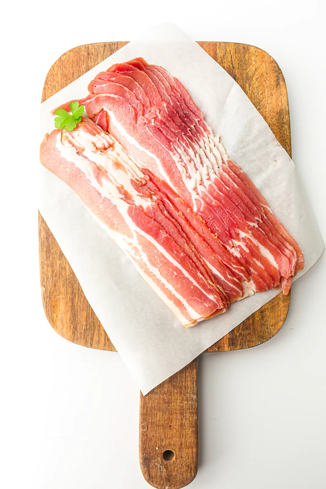 Air fryer bacon ingredients: raw streaky rashers on parchment over a wooden board