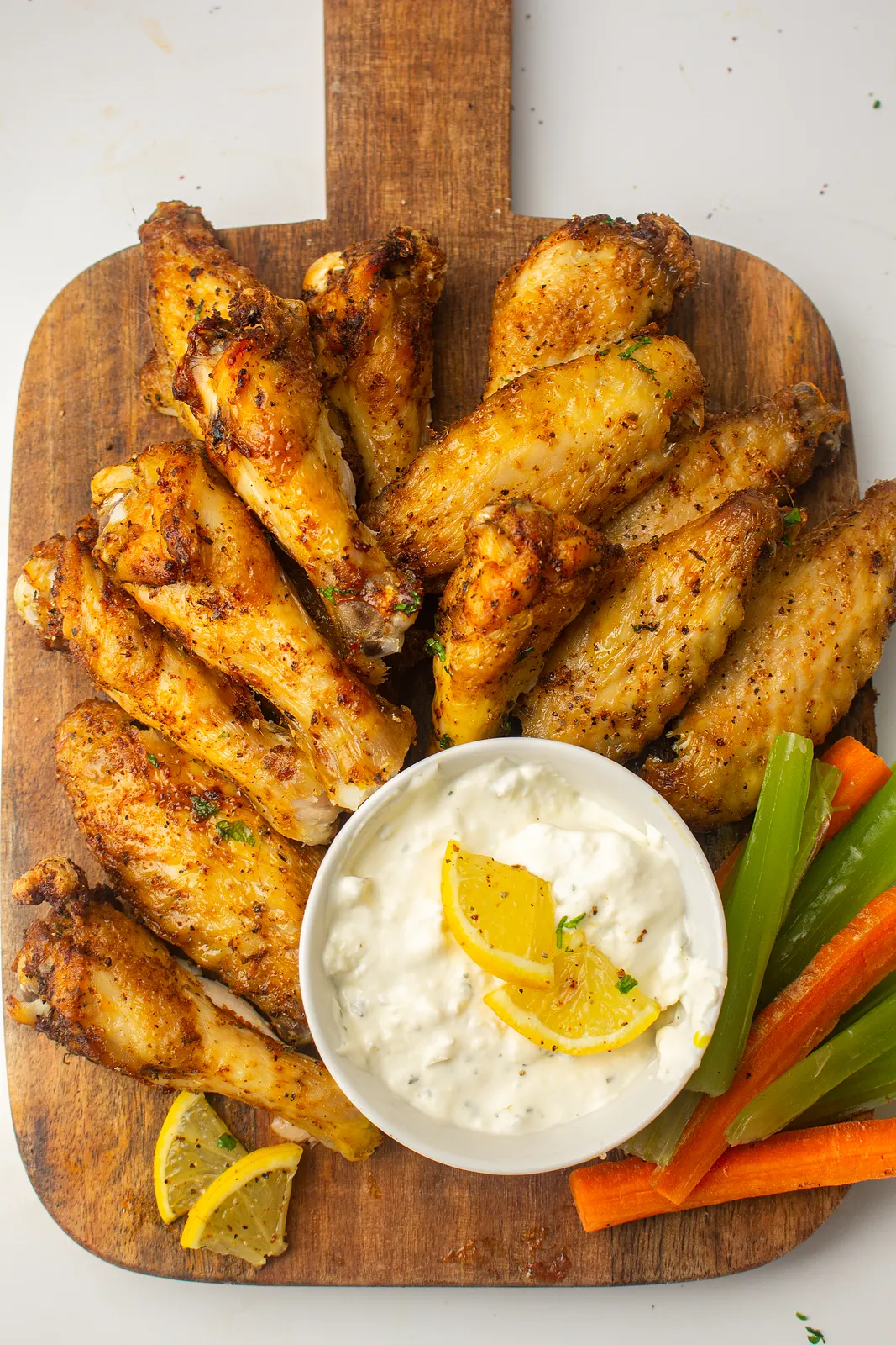 Air fryer chicken wings on a wooden board with a creamy dip, lemon and celery sticks