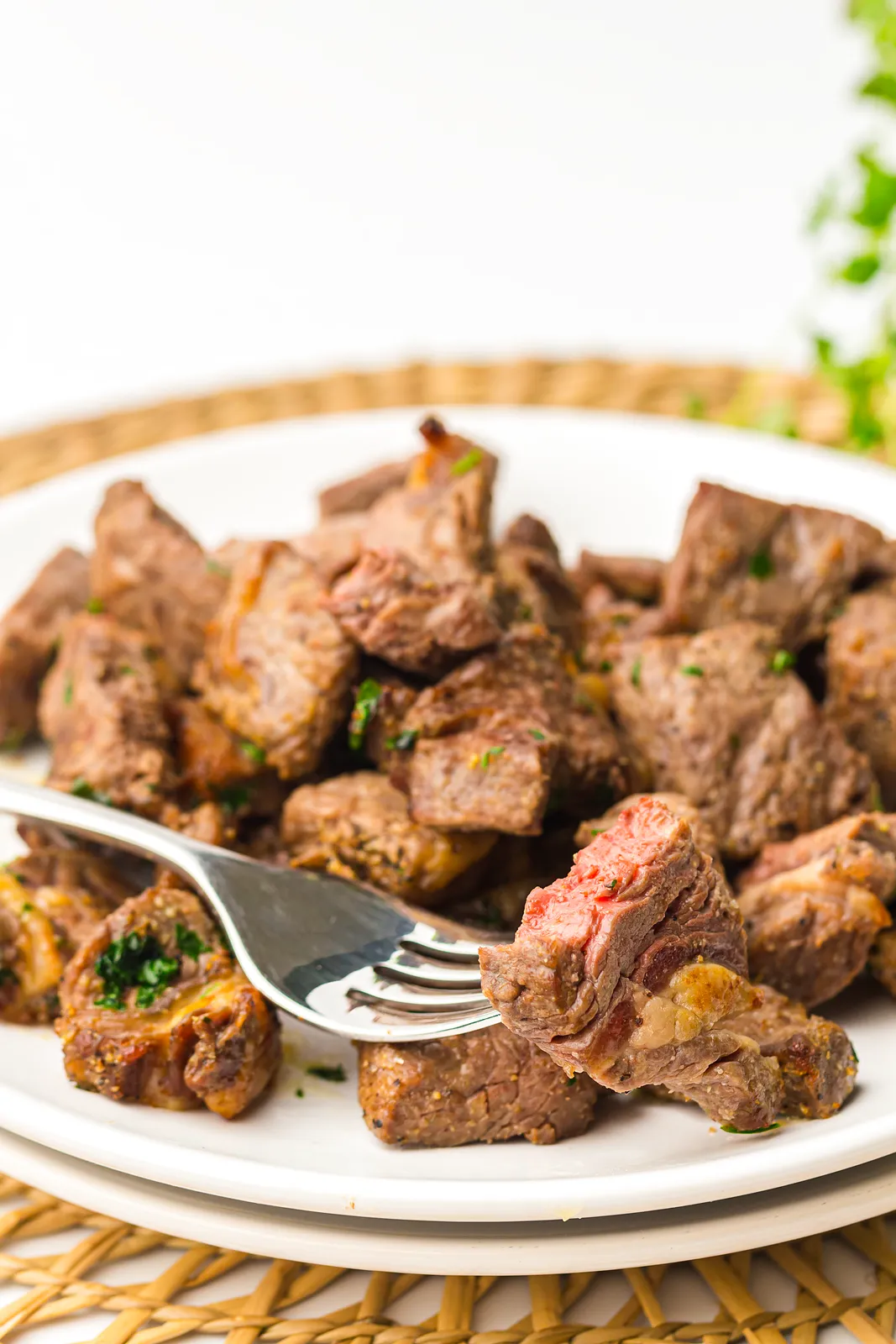 Air fryer steak bites on a white plate with a fork lifting a pink centred piece