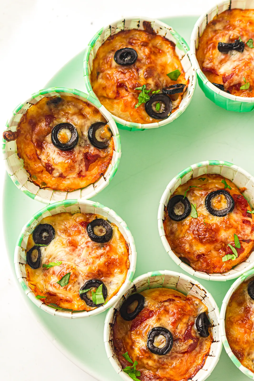 Golden baked dough cups with olives in green paper cases on a mint plate
