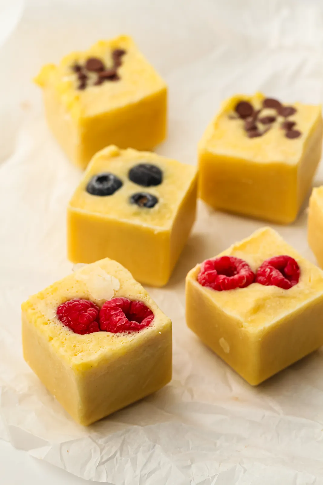 Yellow batter cubes topped with raspberries, blueberries and chocolate chips on parchment