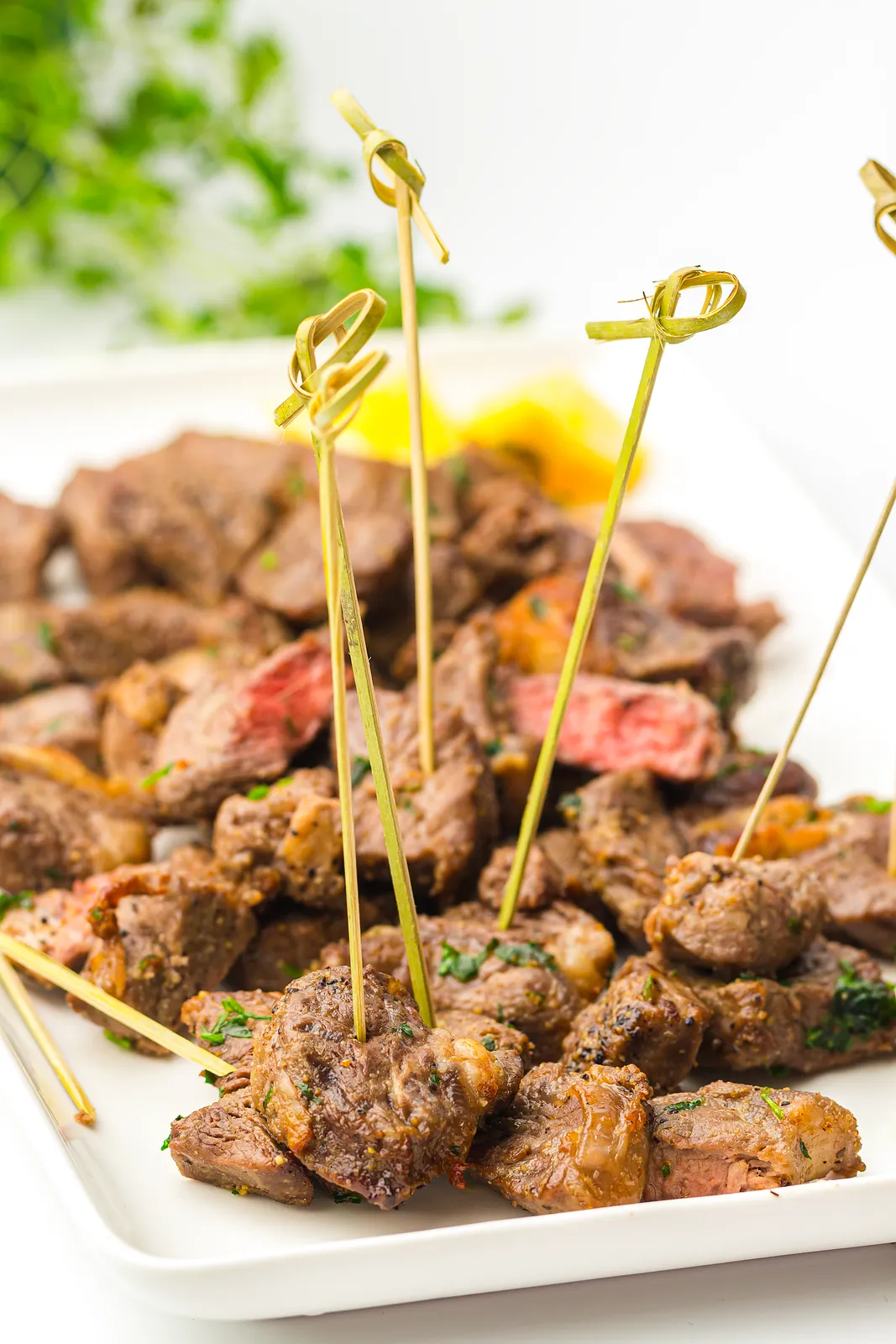 Beef cubes speared on knotted bamboo cocktail picks on a white serving plate