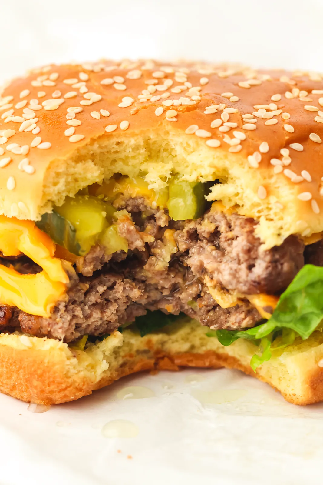 A cheeseburger with a bite taken out showing the thin patty and pickles