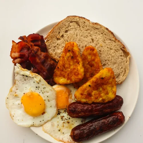 Blackstone breakfast plate with crispy bacon, sausages, hash brown triangles, a fried egg and toast