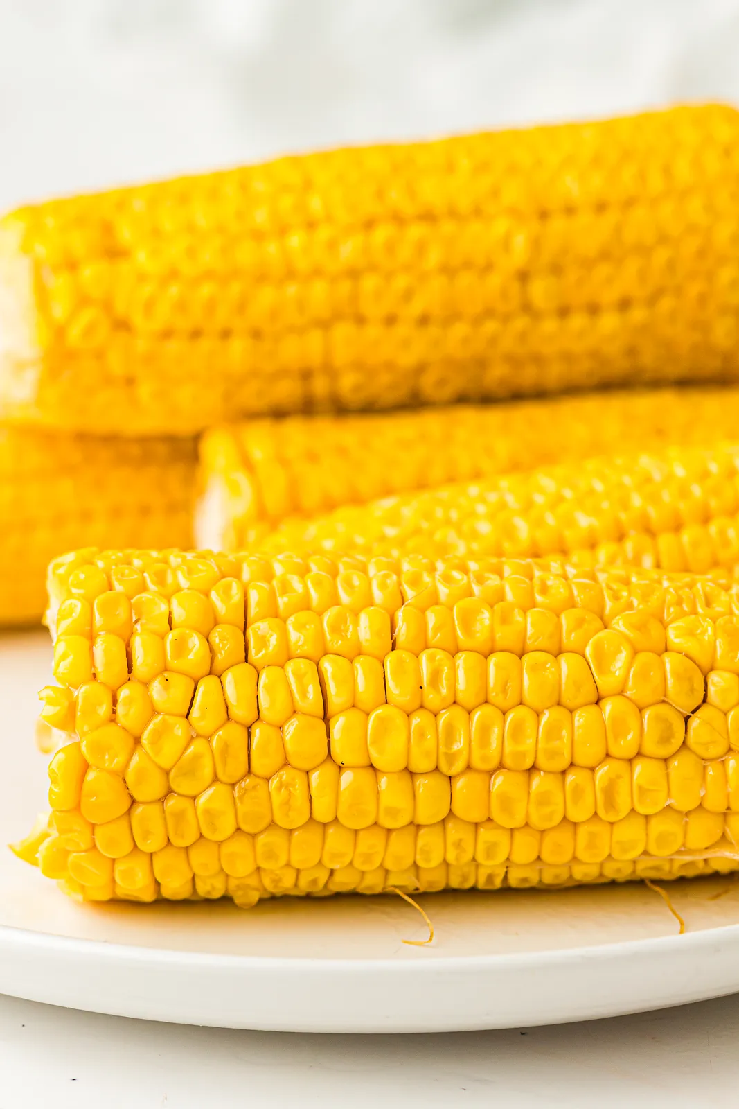 Boiled corn on the cob, four golden ears stacked on a white plate