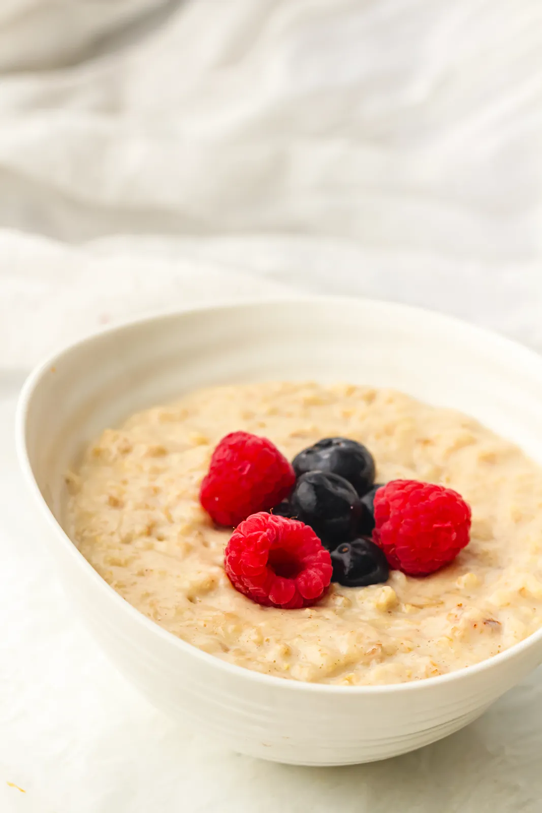 A white bowl of creamy porridge topped with raspberries and blueberries