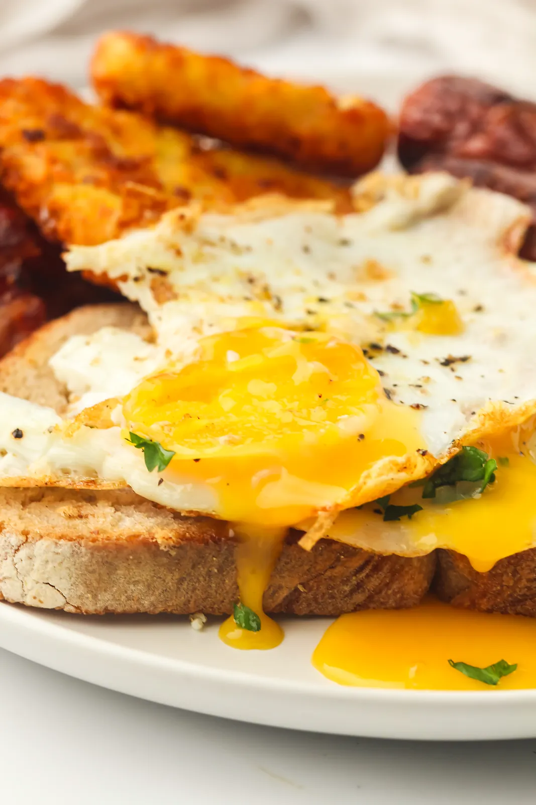 A broken egg yolk spilling over griddled toast with golden potatoes behind