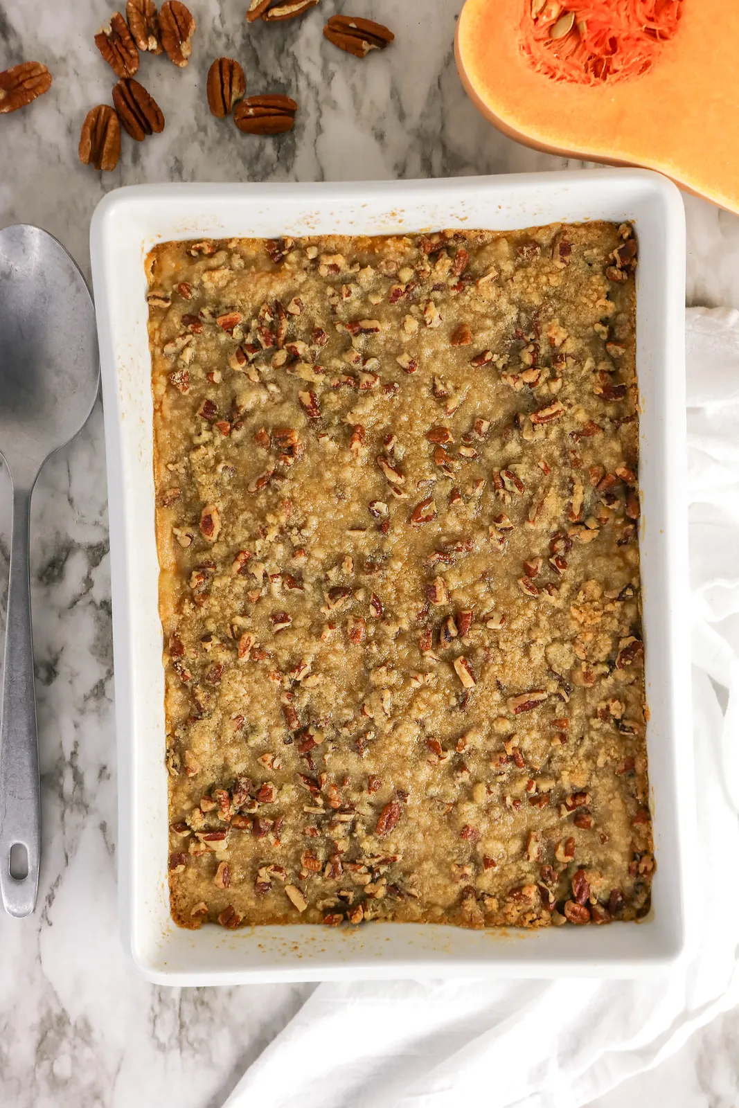 Butternut squash casserole with a pecan crumble topping in a white baking dish