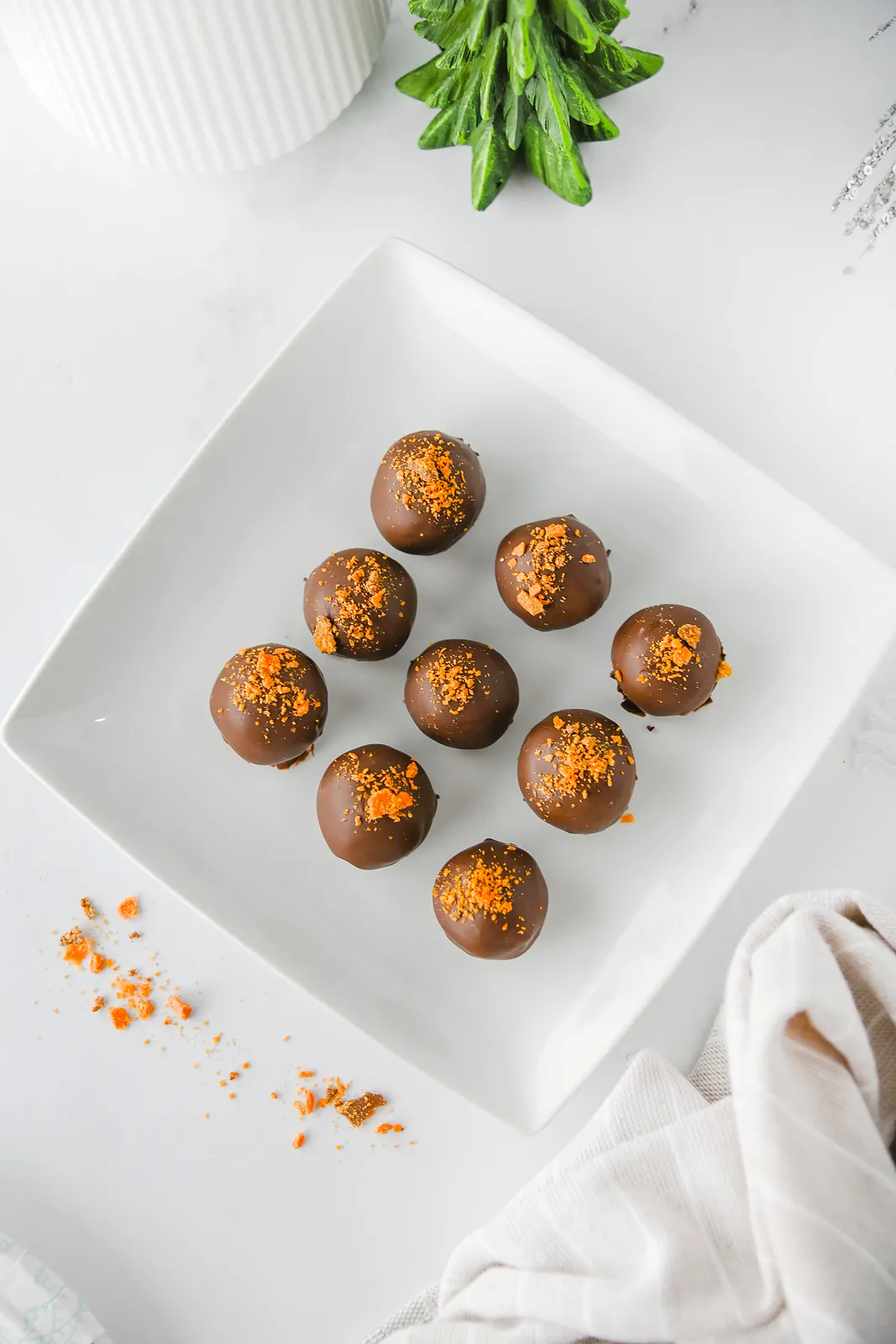 Nine chocolate candies with orange crumbs on a square plate from above