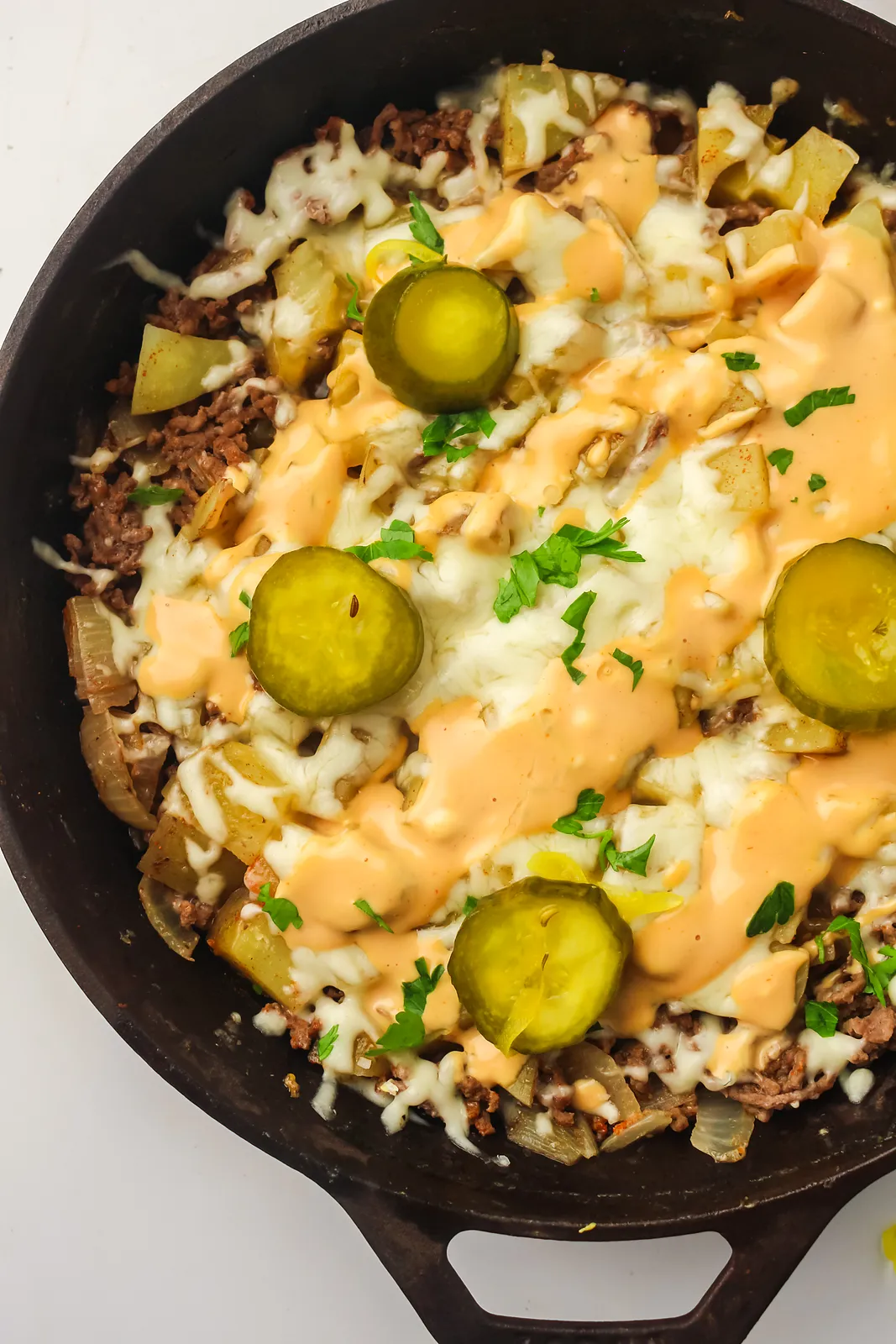 Cheeseburger skillet with ground beef, potatoes, melted cheese, burger sauce and pickles in a cast iron pan