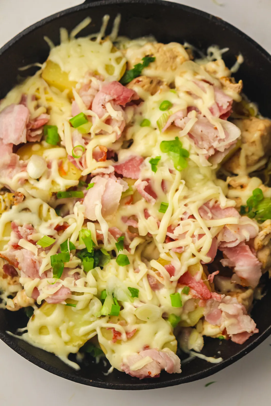 Cast iron pan of melted cheese, tender potatoes and green onion