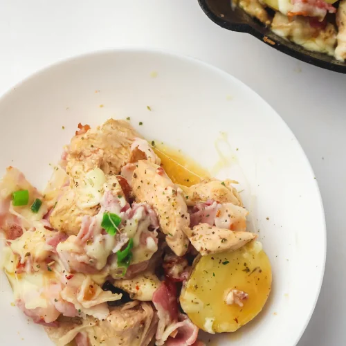 Chicken bacon ranch with potatoes and melted cheese in a white bowl beside the skillet
