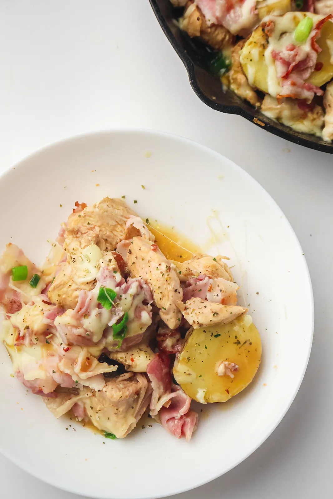 Chicken bacon ranch with potatoes and melted cheese in a white bowl beside the skillet