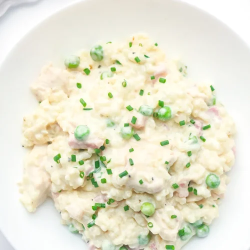 Creamy chicken risotto with bacon, peas and chives in a white bowl