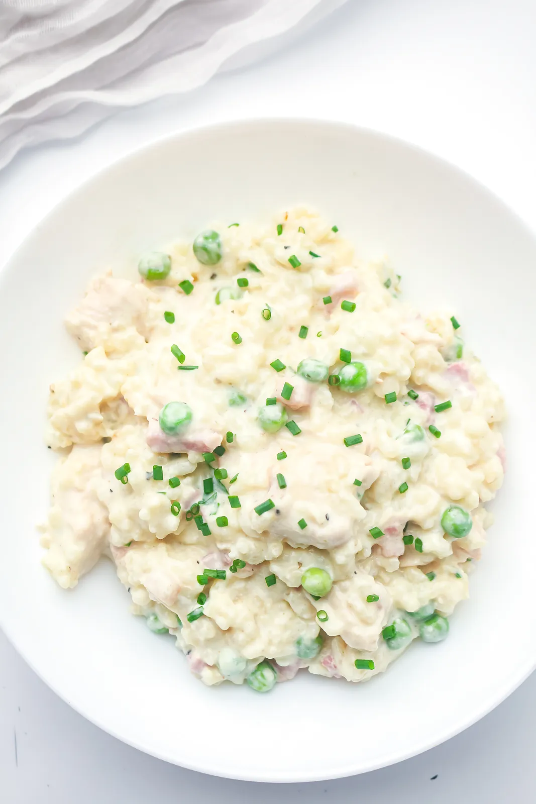 Creamy chicken risotto with bacon, peas and chives in a white bowl